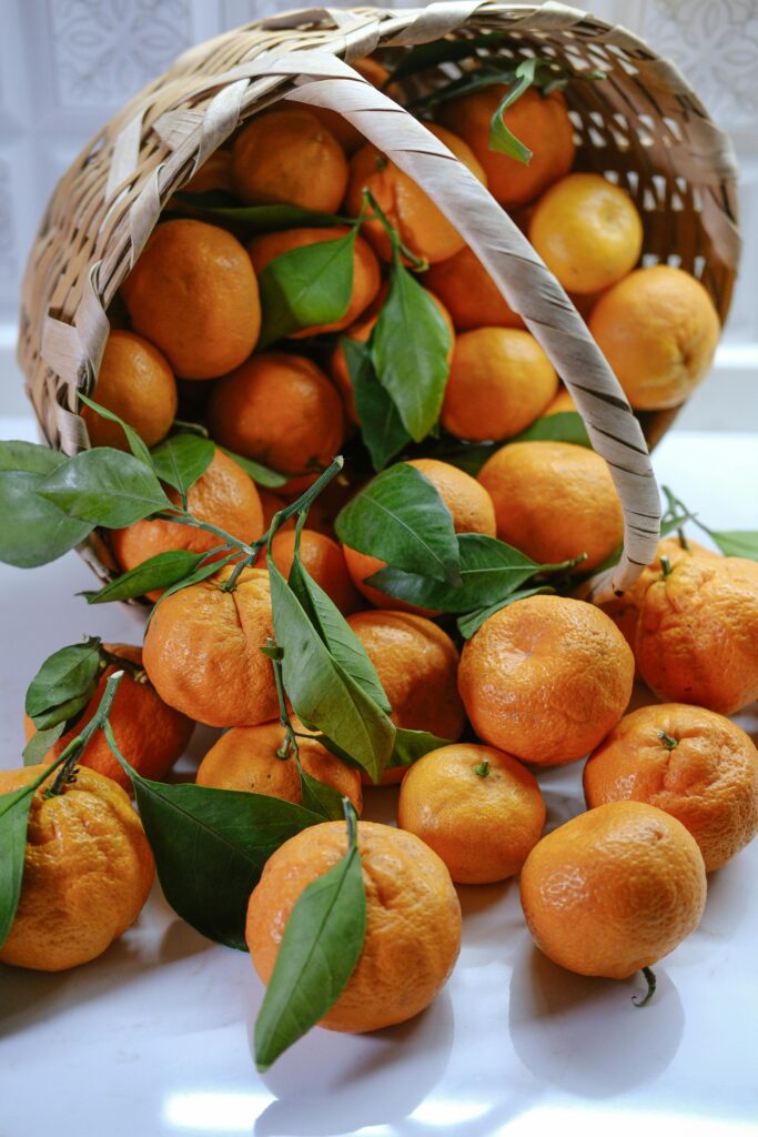 Vibrant and fresh tangerines with green leaves spilling from a woven basket.